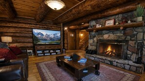 A log cabin interior with a stone fireplace, a mounted television, leather furniture, and a wooden ceiling. - Rustic & Spacious Log Cabin w/Private Hot Tub, Amazing Views, 4 Miles to Ski (Durango)