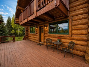 A log cabin with a deck, a balcony, and a table with chairs.