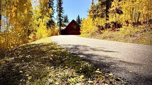 A gravel road leading to a red cabin surrounded by autumn foliage. - Rustic & Spacious Log Cabin w/Private Hot Tub, Amazing Views, 4 Miles to Ski (Durango)