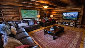A log cabin interior with a leather sofa, a coffee table, a TV, and a fireplace. - Rustic & Spacious Log Cabin w/Private Hot Tub, Amazing Views, 4 Miles to Ski (Durango)