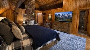 A log cabin bedroom with a bed, a television, a stone wall, and a wooden ceiling. - Rustic & Spacious Log Cabin w/Private Hot Tub, Amazing Views, 4 Miles to Ski (Durango)