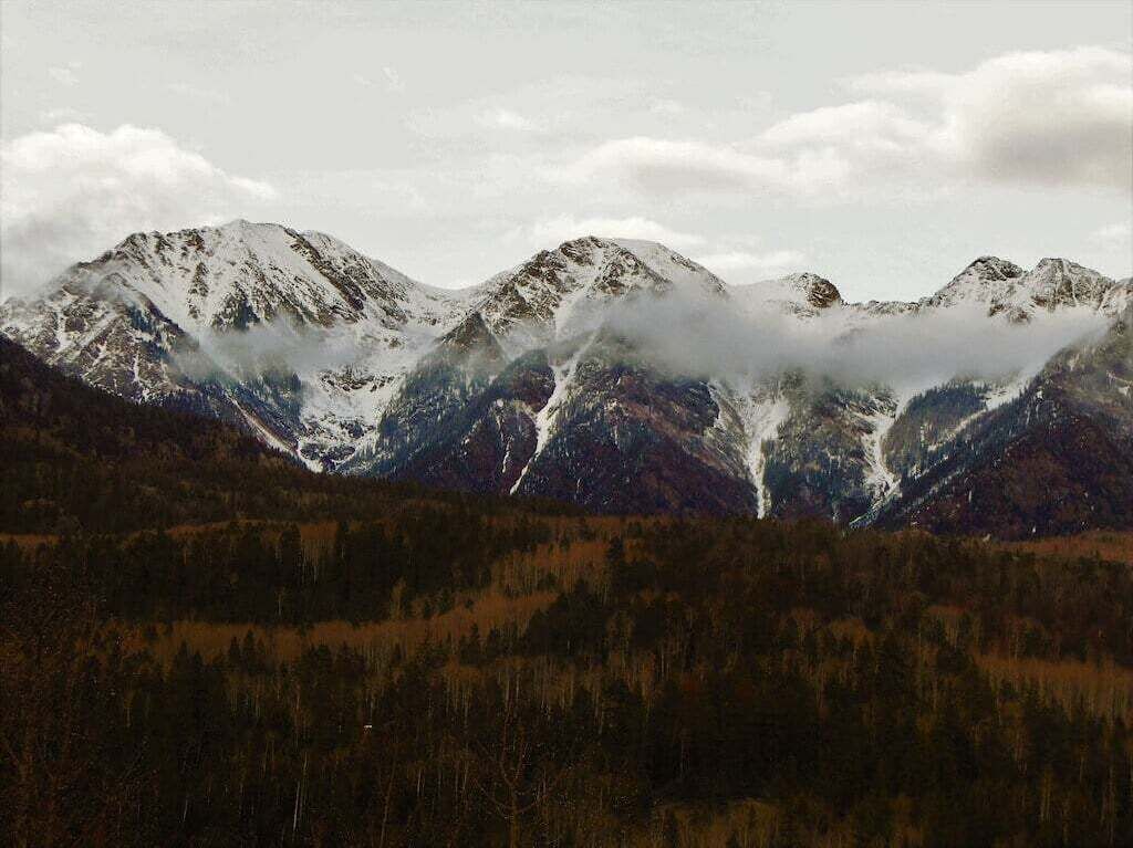A mountain landscape with snow-capped peaks and a forested valley.