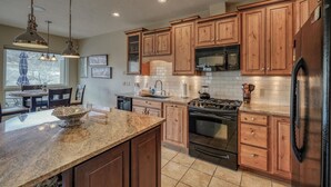 A kitchen with wooden cabinets, a granite countertop, a stove, a microwave, and a refrigerator.