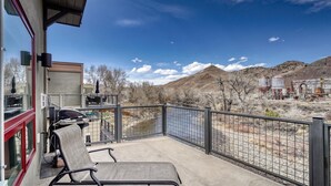 A balcony with two chairs, a grill, and a view of a river and mountains.