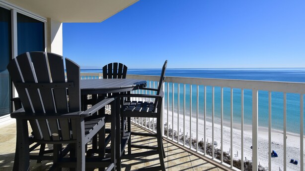 A balcony with a table and two Adirondack chairs overlooking a beach. - Coastal Beachfront Condo w/ Relaxing Community Pool in Destin! 💙☀🌊 (Destin)