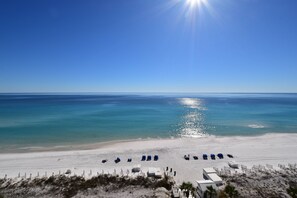 A beach with rows of blue lounge chairs and a white building in the foreground. - Coastal Beachfront Condo w/ Relaxing Community Pool in Destin! 💙☀🌊 (Destin)