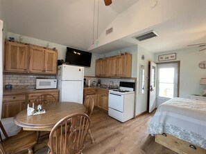 A compact kitchen with wooden cabinets, a microwave, a stove, and a dining area with a table and chairs.