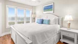 A bedroom with a bed, two bedside tables, a ceiling fan, a window with blinds, and a framed picture on the wall.