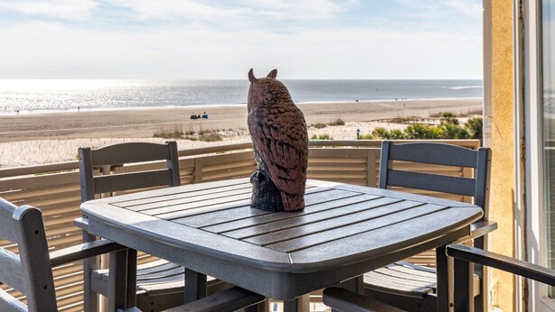 A table and chairs on a balcony overlooking a beach.