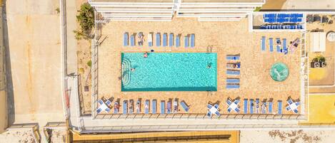 An aerial view of a beachside hotel with a swimming pool, sun loungers, and a lifeguard stand.