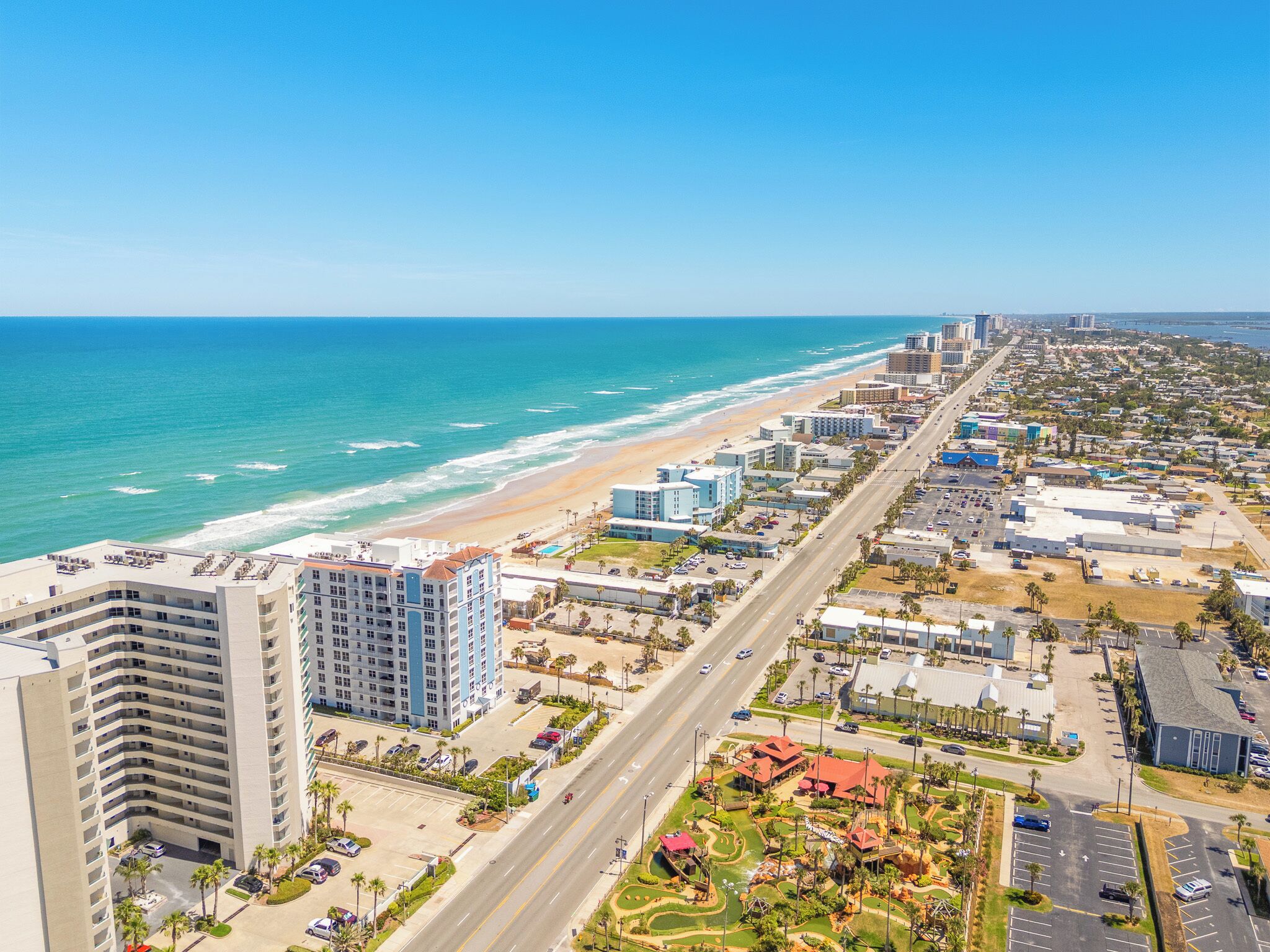 A coastal cityscape with a beachfront hotel, a wide road, and dense urban development.