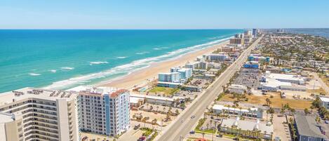 A coastal cityscape with a beachfront hotel, a wide road, and dense urban development.