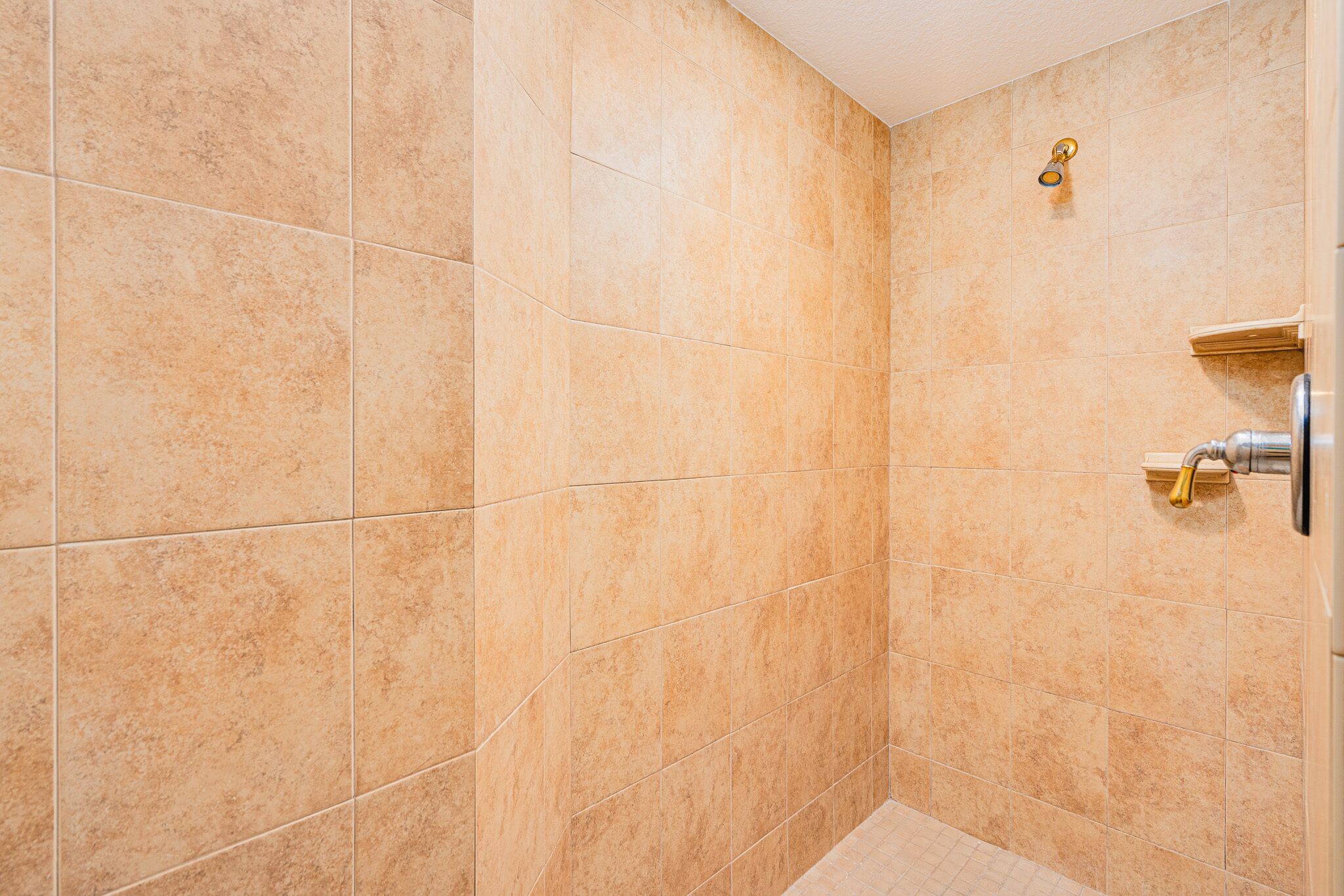 A shower with beige tiles and a gold showerhead.
