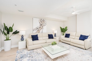 Relax in this stylish living room with a sofa, coffee table, and side tables, surrounded by artwork and lush greenery.