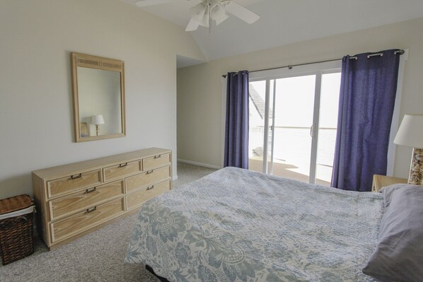 A bedroom with a large bed, a wooden dresser, a mirror, and a view of the outdoors through a sliding glass door. - Large, newly renovated oceanfront home with superb views of Breach Inlet (Sullivan's Island)