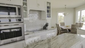 Una cocina con armarios blancos, microondas, horno y encimera de mármol.