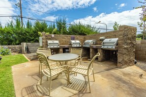 Une terrasse extérieure avec une table ronde et quatre chaises, un mur en pierre et trois barbecues.