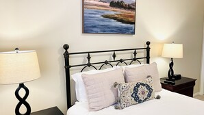 A neatly made bed with white linens and decorative pillows, flanked by two bedside tables with lamps, one on each side.