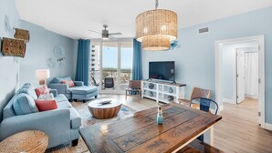 Ein modernes Wohnzimmer mit einem Holztisch, blauen Sofas, einem Fernseher und einem Balkon mit blauen Vorhängen.