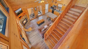 Interior de una cabaña de madera con sala de estar, cocina y una escalera.