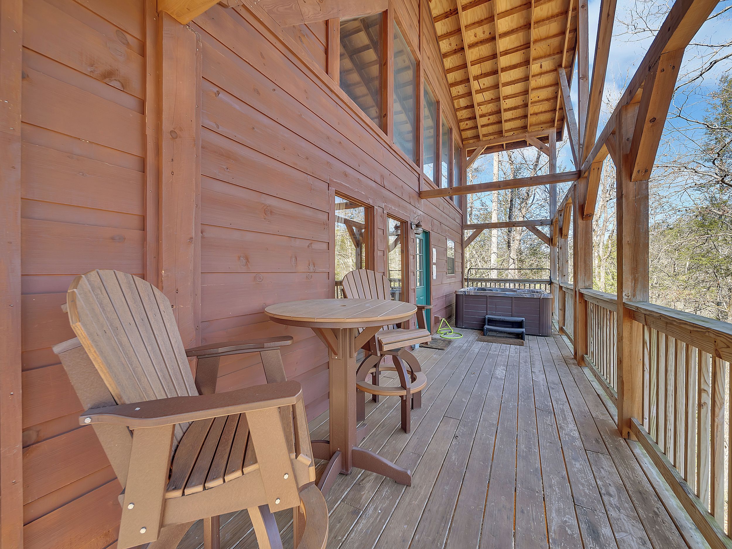 Eine Holzterrasse mit Whirlpool, Tisch und zwei Adirondack-Stühlen.
