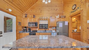 Una cocina con armarios de madera, encimera de granito, electrodomésticos de acero inoxidable y techo de madera.