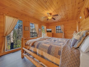 A wooden cabin bedroom with a bed, a ceiling fan, and large windows.