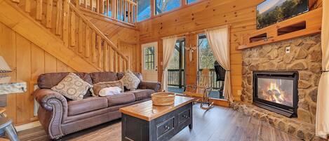 L’intérieur d’un chalet en bois, avec un escalier, une cheminée, un canapé et une table à manger.