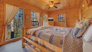 Un dormitorio de cabaña de madera con una cama, un ventilador de techo y ventanas amplias.