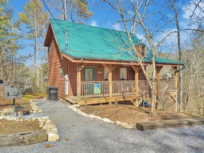 A wooden cabin with a green roof, a porch, and a sign advertising a restaurant. - Private Hot Tub | Seclusion | Pool Table | Pet Friendly (SEVIERVILLE)