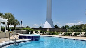 Piscina com uma estrutura alta, branca e cilíndrica, com topo esférico, rodeada por espreguiçadeiras e uma pérgula branca.
