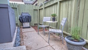 Un patio con una parrilla, dos sillas, una mesita y una planta en maceta.