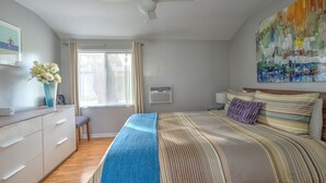 Un dormitorio con cama, escritorio, silla, ventana con cortinas, ventilador de techo y aire acondicionado instalado en la pared.