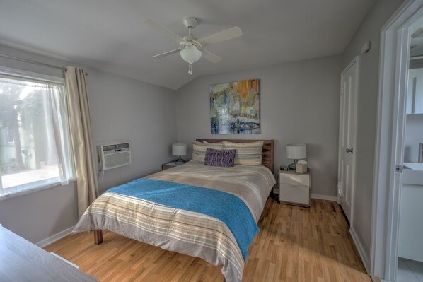 A bedroom with a bed, bedside tables, a ceiling fan, a window with curtains, and a painting on the wall.