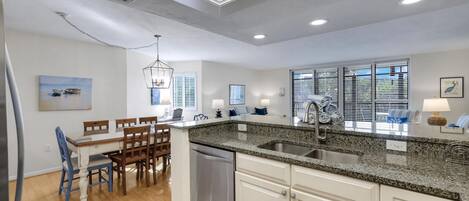 A modern kitchen with granite countertops, a built-in dishwasher, and a dining area with wooden chairs and a table.