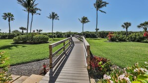 A wooden boardwalk leading through a well-maintained garden with palm trees and flowering plants. - COMPASS POINT 221- Your Beach Getaway! (Sanibel)