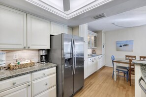 Una cocina moderna con muebles blancos, un refrigerador de acero inoxidable, una cafetera y un comedor con mesa y sillas.