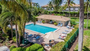 A pool area with lounge chairs and umbrellas, surrounded by palm trees and a building with a tiled roof. - COMPASS POINT 221- Your Beach Getaway! (Sanibel)