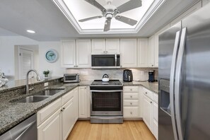 A modern kitchen with white cabinets, stainless steel appliances, a built-in microwave, a gas stove, and a ceiling fan.