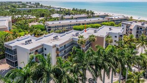 A multi-story hotel with a rooftop pool area, surrounded by palm trees and a beach view. - COMPASS POINT 221- Your Beach Getaway! (Sanibel)