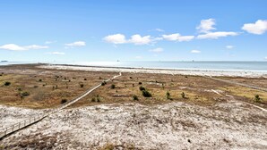 A coastal landscape with a sandy beach, a dirt path, and a distant shoreline.