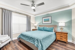 A bedroom with a bed, two nightstands, a ceiling fan, and a window with curtains. - Ocean Song 332 | Oceanfront, Amazing Views! (Tybee Island)