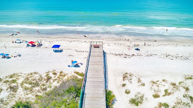 A beach with a wooden pier leading to the shore, surrounded by sand and sparse vegetation. - Savor Gulf Views! 3/3 Heated Pool/Spa, Beachside - 603 (Redington Shores)