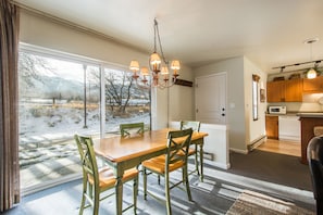 A dining area with a wooden table and chairs, a chandelier, and a view of a snowy landscape through large windows.