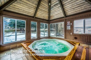 A large wooden interior with a hot tub, large windows, and a view of a snowy landscape.