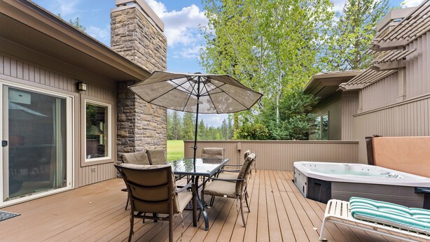 Una terraza de madera con un jacuzzi, una mesa con sillas y una sombrilla.