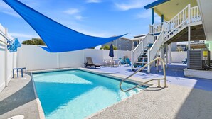 Una piscina con una toldo azul, una escalera y mobiliario de exterior.