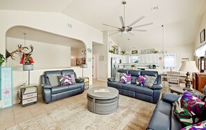 A spacious living room with a fireplace, a ceiling fan, and a view into the kitchen.