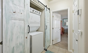 Un lavadero con lavadora y secadora, una puerta corredera y un pasillo que conduce a otra habitación.