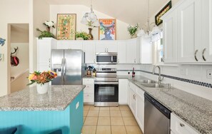 Una cocina moderna con armarios blancos, electrodomésticos de acero inoxidable, encimera de granito y una isla azul.